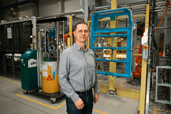 Lukáš Mildorf, CTO hos Teijin Automotive Technologies Czech s.r.o., står foran produktionslinjen for batteridæksler. I baggrunden ses en Robatech RobaDrum 20 klæbemiddelsmelter.